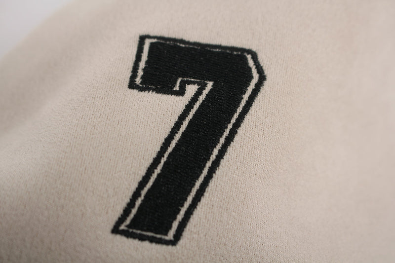 Close-up of a black embroidered number 7 on a cream athletic streetwear tee