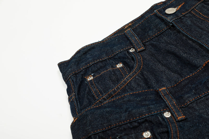 Close-up of the front pocket area on deep indigo jeans with snap details and contrast stitching