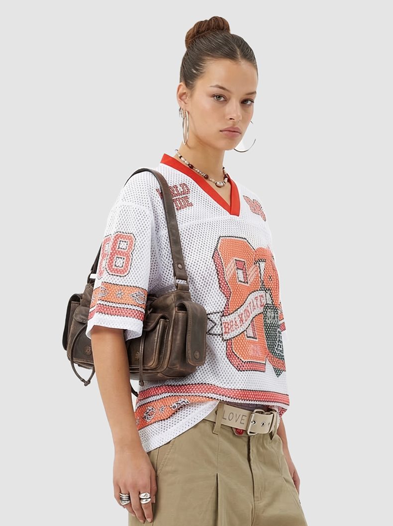 Model wearing a white mesh varsity jersey with orange trim and 88 graphic, paired with khaki pants and a brown shoulder bag