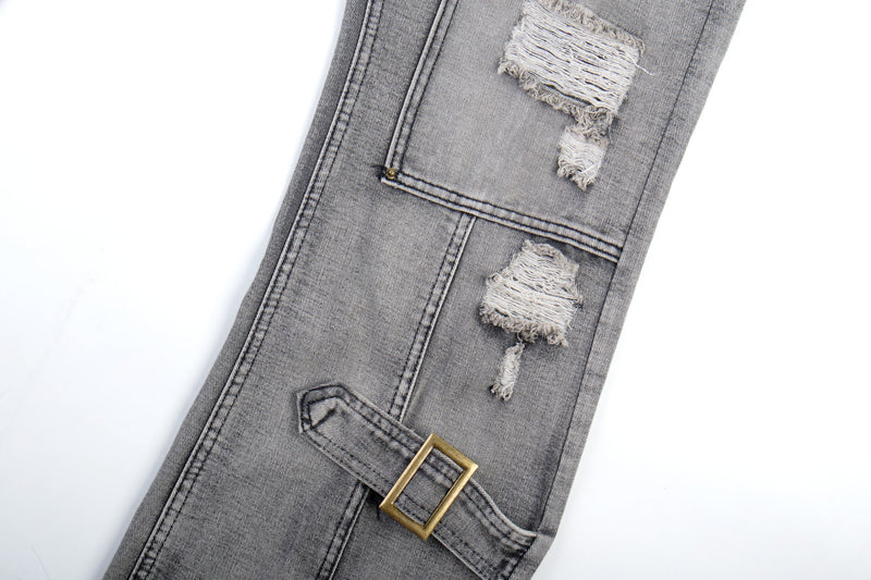 Side leg close-up of grey distressed jeans with frayed rip patches and buckle strap