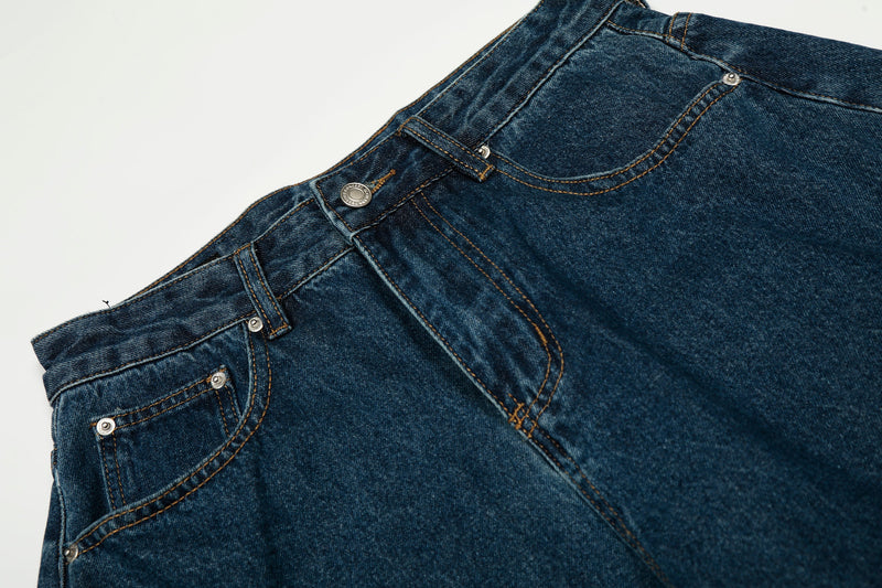 Close-up of the front waistband, button closure, and pocket stitching on dark indigo jeans