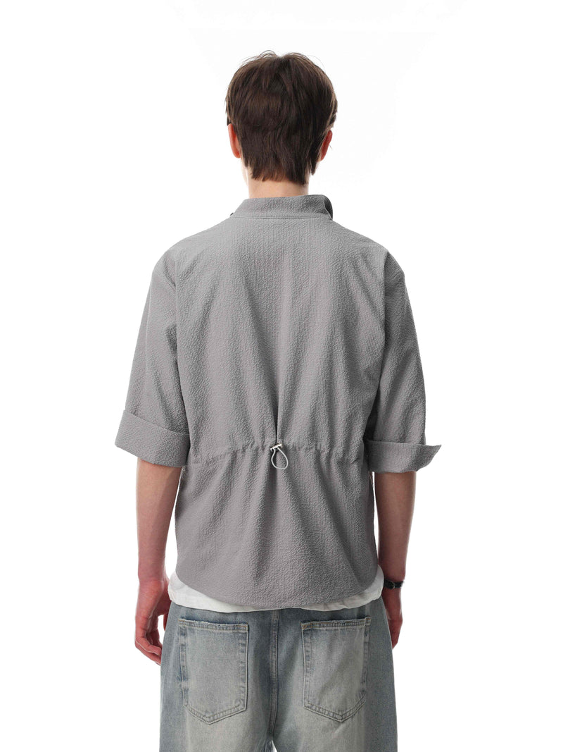 Back view of a gray textured stand-collar shirt with rolled sleeves and drawstring detail, styled with light jeans
