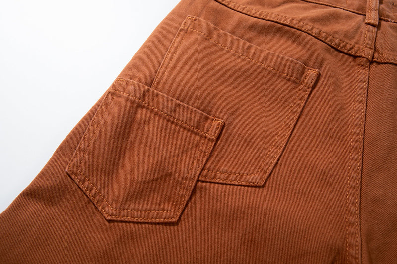 Close-up of a curved side pocket on rust brown jeans with topstitching detail