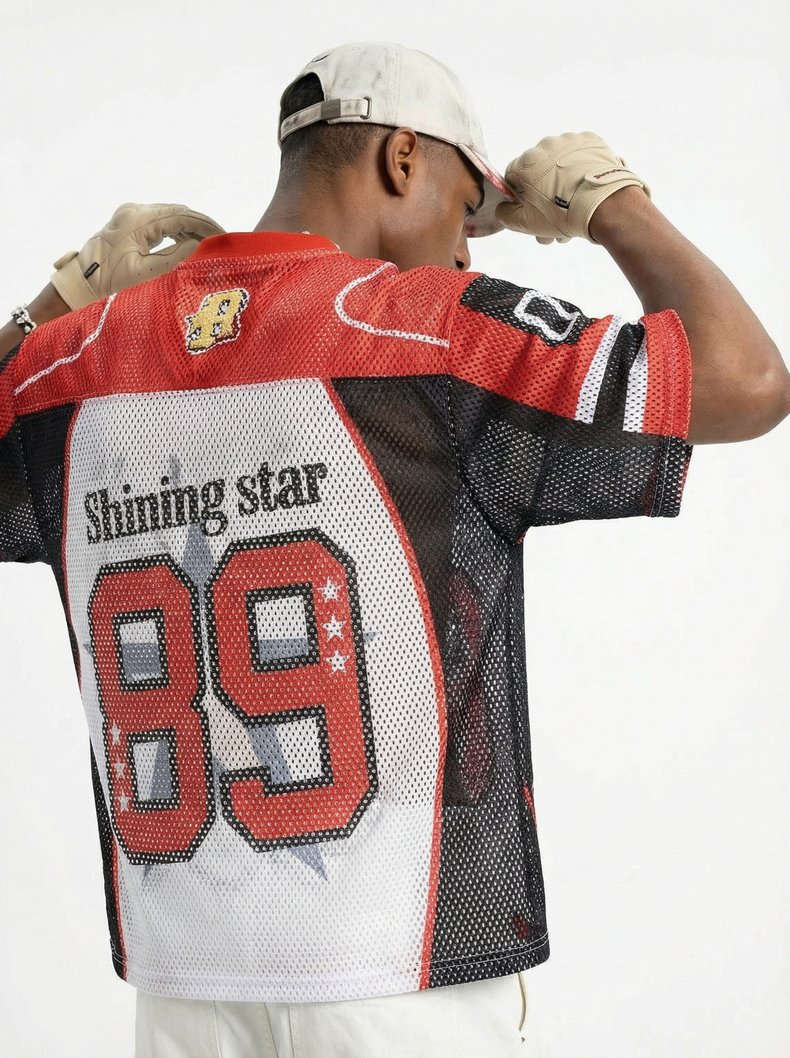 Man wearing a red, black and white mesh football jersey with 89 graphic on the back and streetwear styling