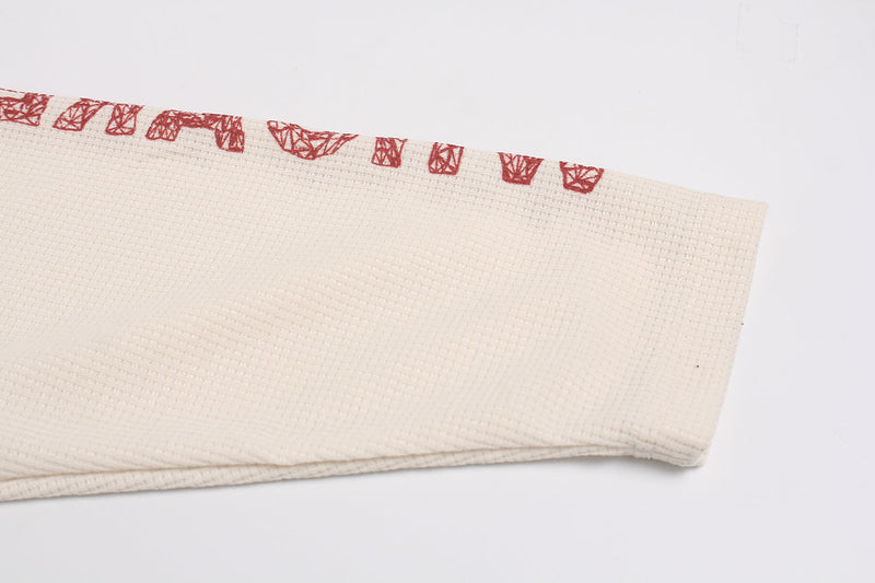 Cream waffle-knit sleeve hem with small red geometric trim detail