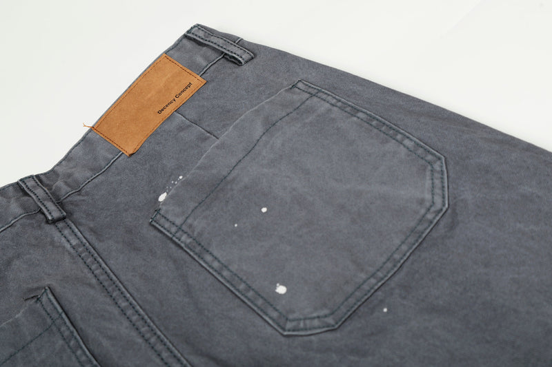 Close-up of back pocket on gray jeans with tan label patch and scattered white paint splatters