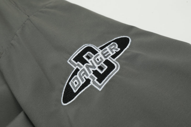 Close-up of sleeve patch on dark gray windbreaker with stitched letter design