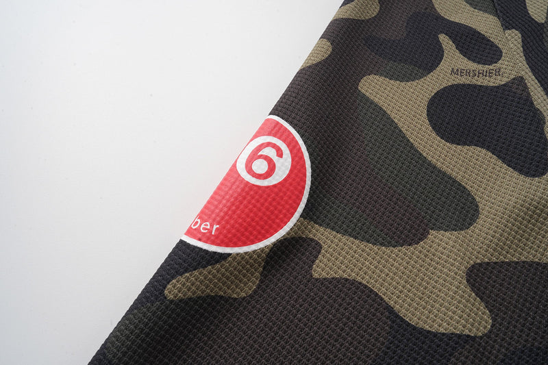 Camo sleeve close-up with red circular 6 patch and black printed branding