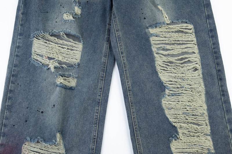 Close-up of front leg distressing with large shredded rips on faded blue jeans