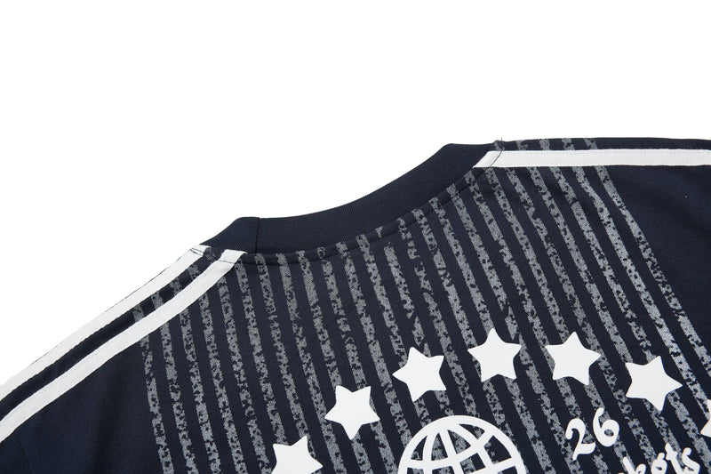 Close-up of a navy sport tee with white shoulder stripes, vertical distressed lines, stars, and graphic lettering on the chest