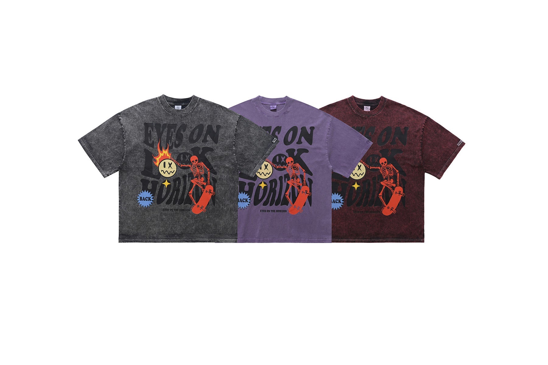 Three acid-washed graphic tees in charcoal, purple, and burgundy featuring a skeleton skater and flaming smiley print