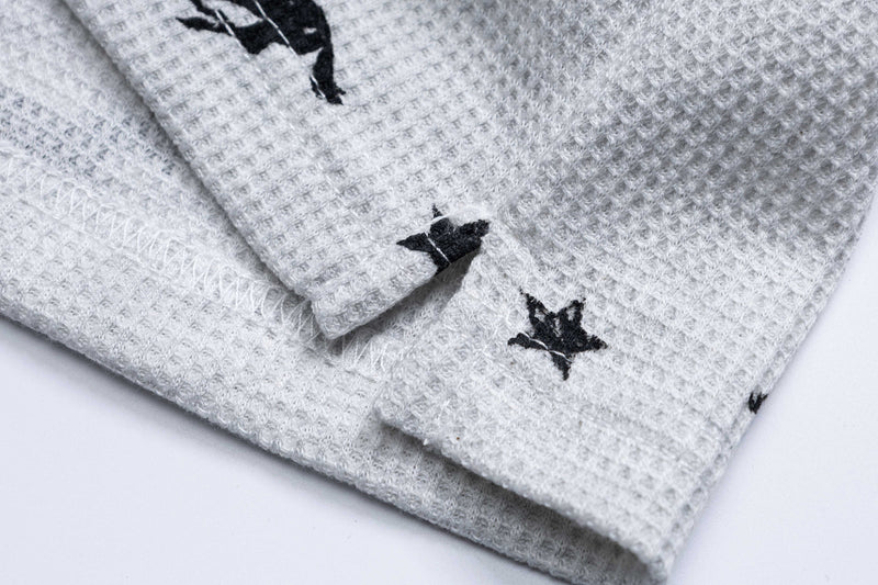 Close-up of a light gray waffle-knit polo tee with black embroidered horse graphics and folded cuffs