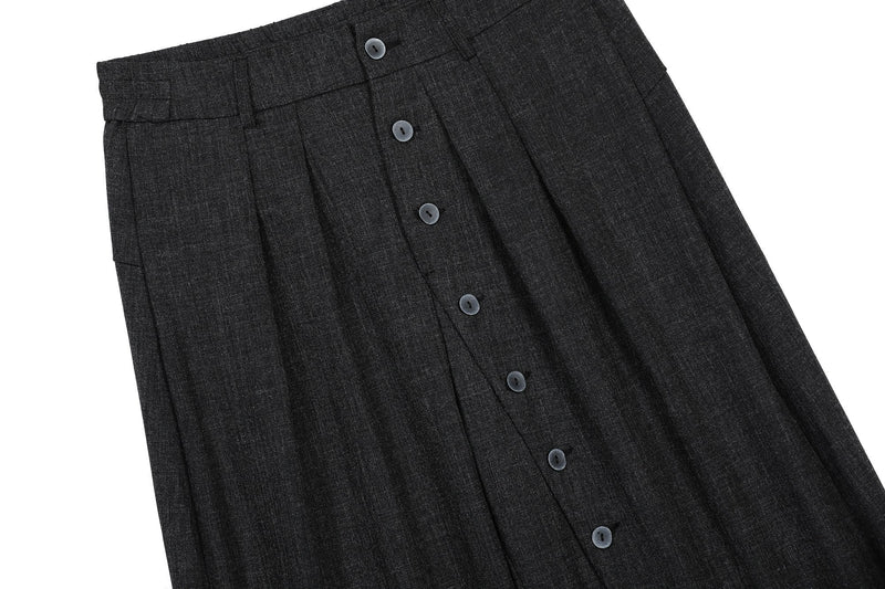 Diagonal close-up of black pants front with pleats and button placket