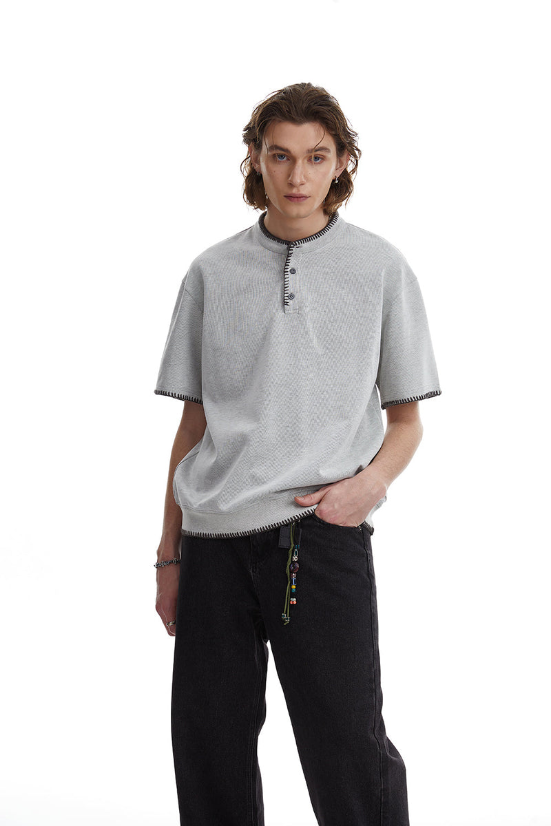 Light gray contrast stitch Henley tee with short sleeves, worn with black relaxed-fit pants on a male model