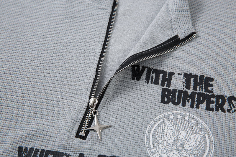 Close-up of a gray half-zip graphic streetwear T-shirt with distressed black print and star-shaped zipper pull detail
