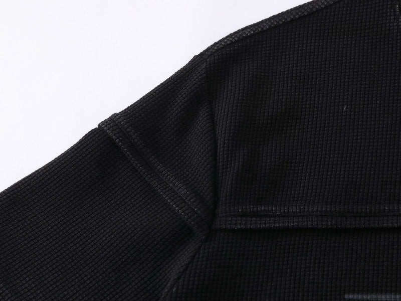 Black waffle knit T-shirt with long sleeves, close-up of textured fabric and seam details on a white background
