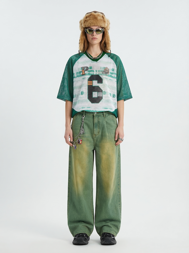 Model wearing a green mesh varsity jersey T-shirt with a large number 6, olive wide-leg pants, and a fur trapper hat