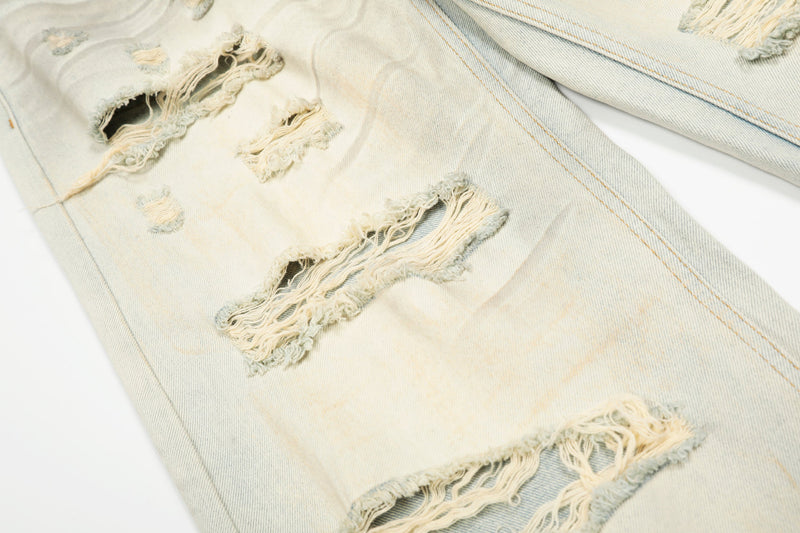 Close-up of ripped holes and heavy distressing on cream denim jeans