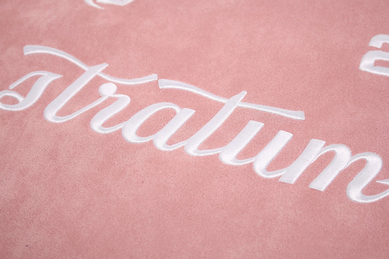 Close-up of pink suede tee fabric with raised white Stratum lettering and sporty streetwear graphic print