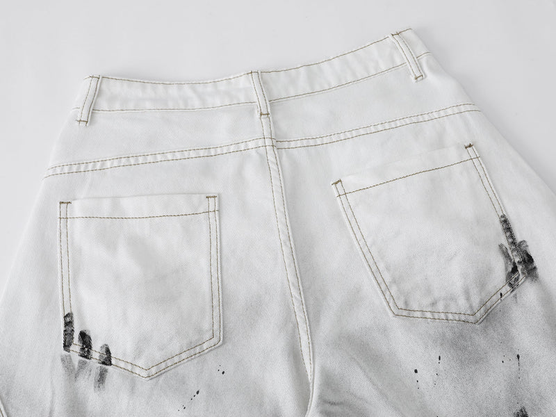 Close-up of the back waistband and patch pockets on white denim shorts with black paint marks