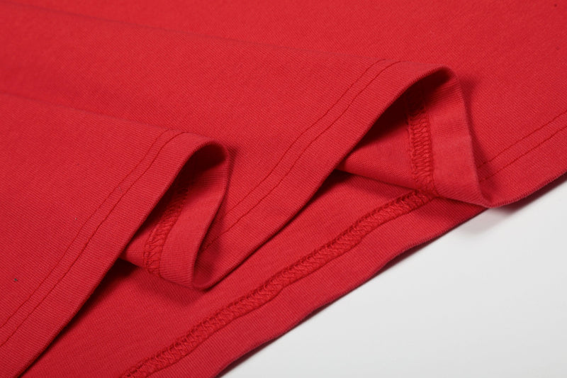 Close-up of a vintage distressed red graphic tee hem with visible stitching and folded cotton fabric texture