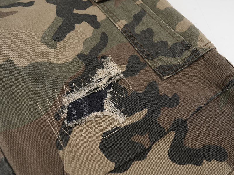 Close-up of ripped camo shorts showing frayed hole and stitched patch layers