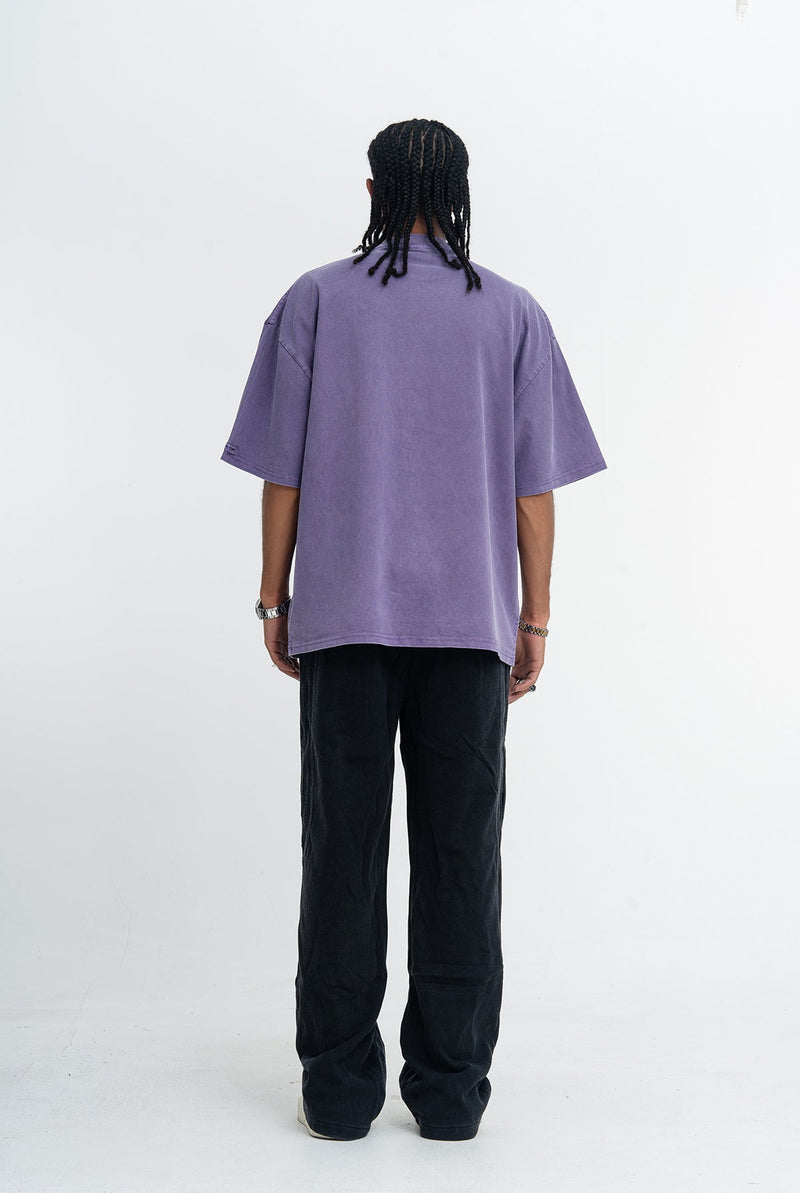 Back view of a loose vintage wash purple skate graphic tee worn with black pants and braids