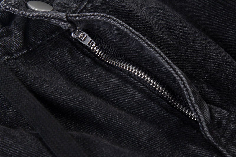 Close-up of black denim zipper fly with snap button at the waistband