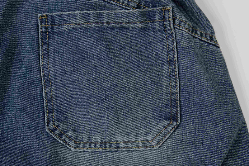 Close-up of blue denim back pocket with contrast stitching on layered plaid jeans