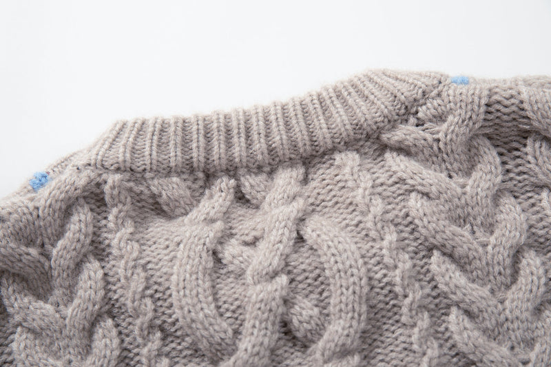 Close-up of beige ribbed crew neckline with cable knit texture and small blue stitch detail