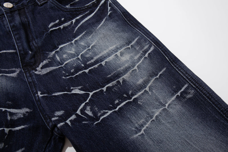 Close-up of the upper front leg on deep indigo jeans with cracked-wash fading and whiskering