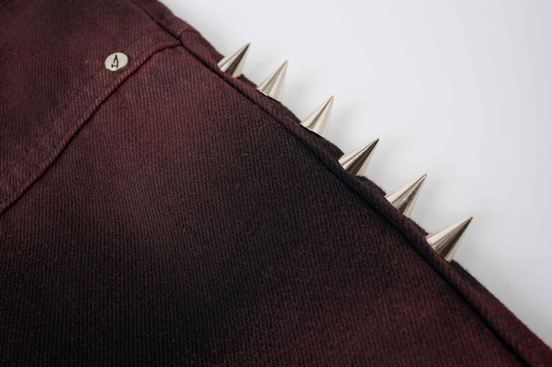 Close-up of burgundy denim side panel with silver cone spikes and seam detail