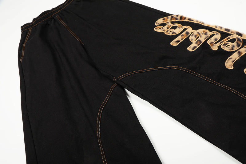 Side view of black wide-leg pants with leopard patch lettering and curved seam stitching