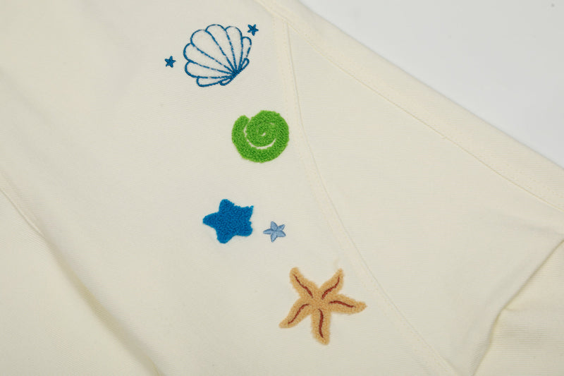 Close-up of cream cargo pants leg with shell, green swirl, and star embroidery