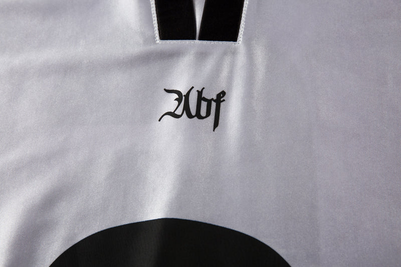 Close-up of white jersey chest with black gothic-style logo under the collar