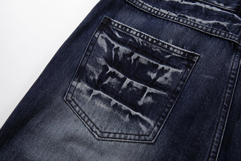 Close-up of one back pocket on deep indigo jeans with cracked-wash fading and contrast stitching