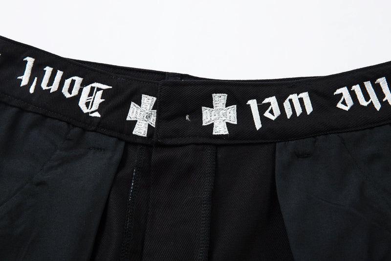 Close-up of the waistband showing white gothic-style text and cross motifs on black fabric