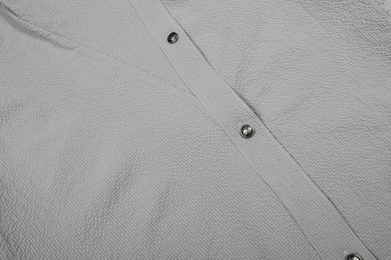 Close-up of a gray asymmetrical cotton shirt with stand collar, textured fabric, and dark button detailing
