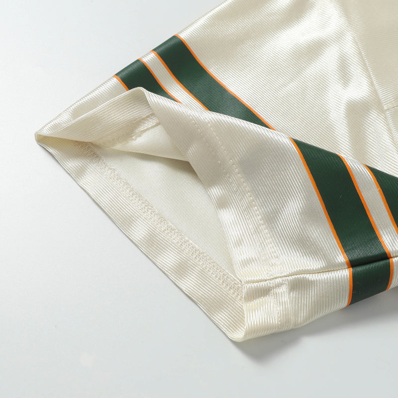 Cream retro football jersey tee with green and orange varsity stripes on textured satin fabric