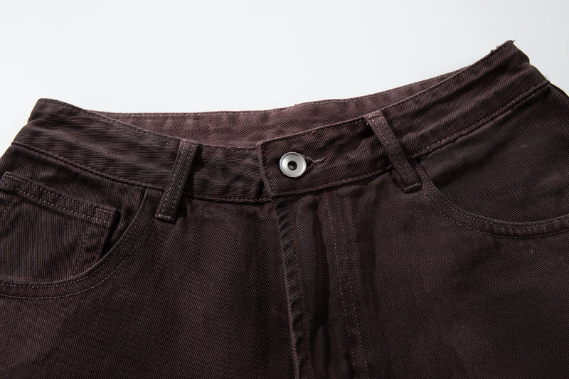 Close-up of brown jeans waistband with button closure, belt loops, and front pockets