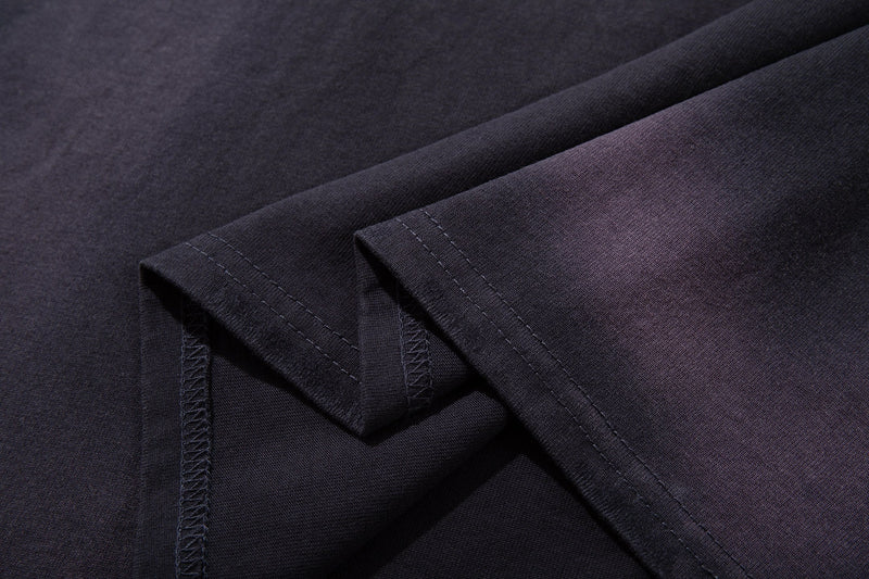 Close-up of dark washed raglan tee fabric with visible stitched hems and a vintage grunge texture