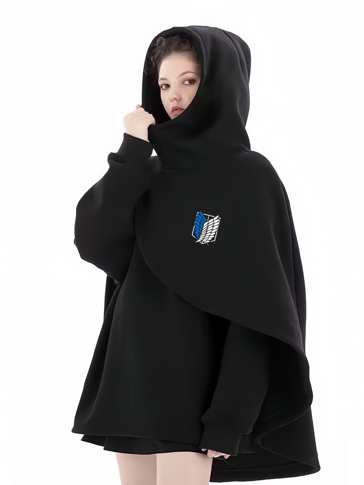 Wearing a Limited Edition Attack on Titan Hooded Cape - Street Style, featuring a blue and white Survey Corps emblem, a person looks forward with the hood up against a plain white backdrop.