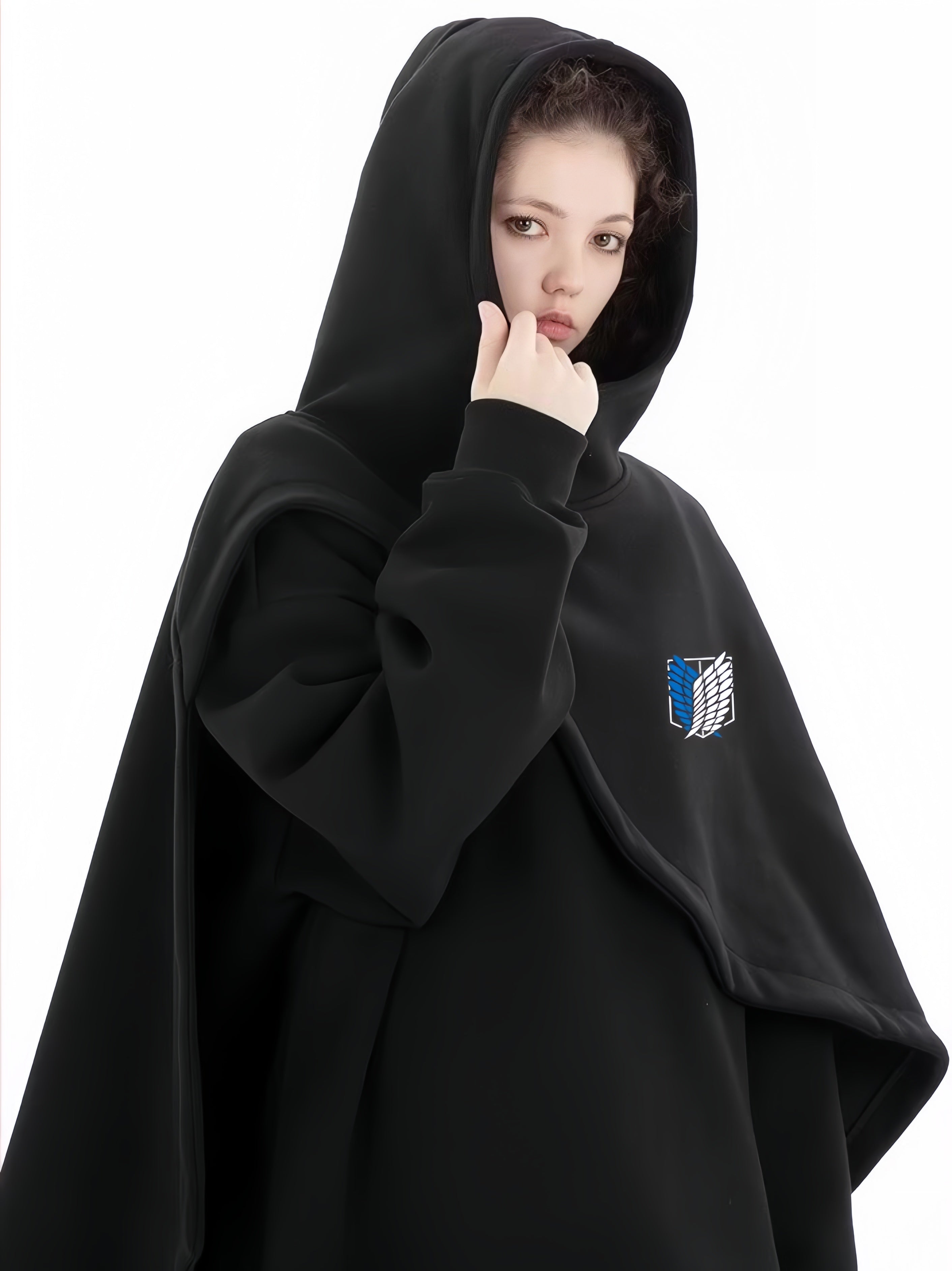 A person wears the Limited Edition Attack on Titan Hooded Cape, featuring the Survey Corps emblem. They adjust the hood and gaze at the camera against a white background, capturing this street-style, thick, and comfortable cape&