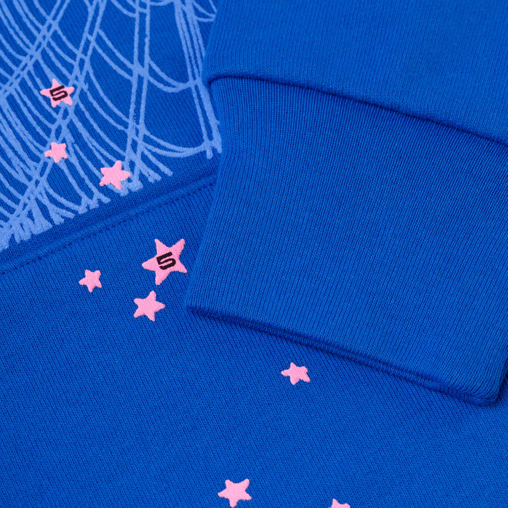 Close-up of the Sp5der “555” Hoodie—Royal Blue 440GSM heavyweight streetwear pullover—showing ribbed cuffs with small pink stars, white web-like lines, and some S-lettered stars inspired by Sp5der’s signature design.