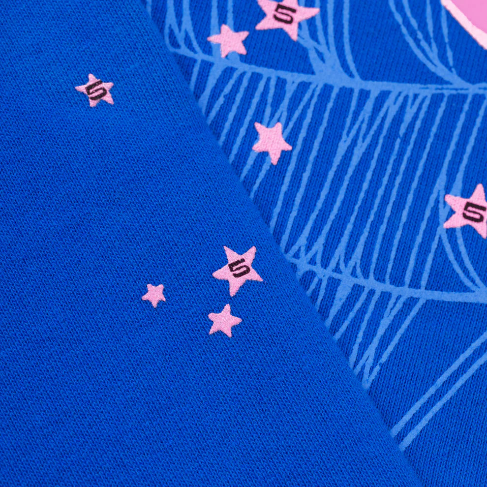 Close-up of blue fabric from the Sp5der “555” Hoodie – Royal Blue 440GSM Heavyweight Spider Web Streetwear Pullover, featuring light pink stars—some with a black number 5—and fine blue line patterns in premium cotton fleece.