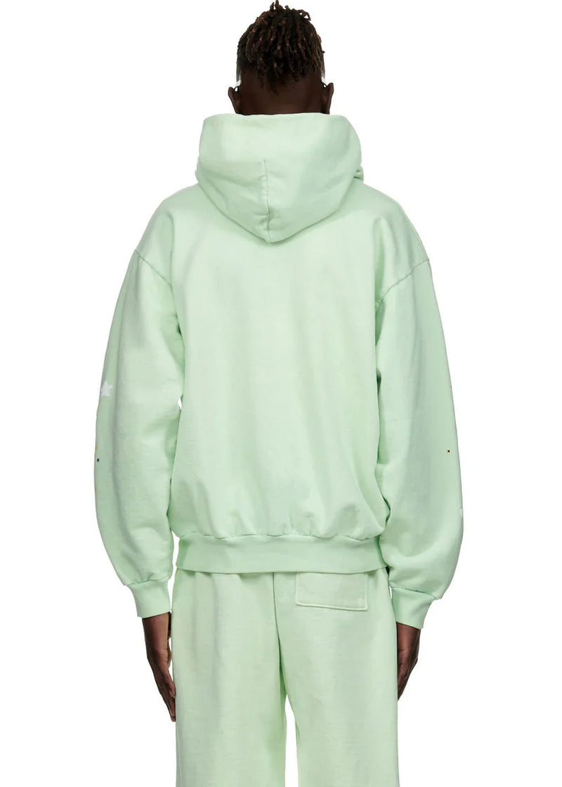 Wearing a Sp5der “Mint Star Web” Hoodie in mint green, a person stands facing away from the camera with arms relaxed, showcasing this 440GSM heavyweight oversized streetwear pullover inspired by Y2K style.