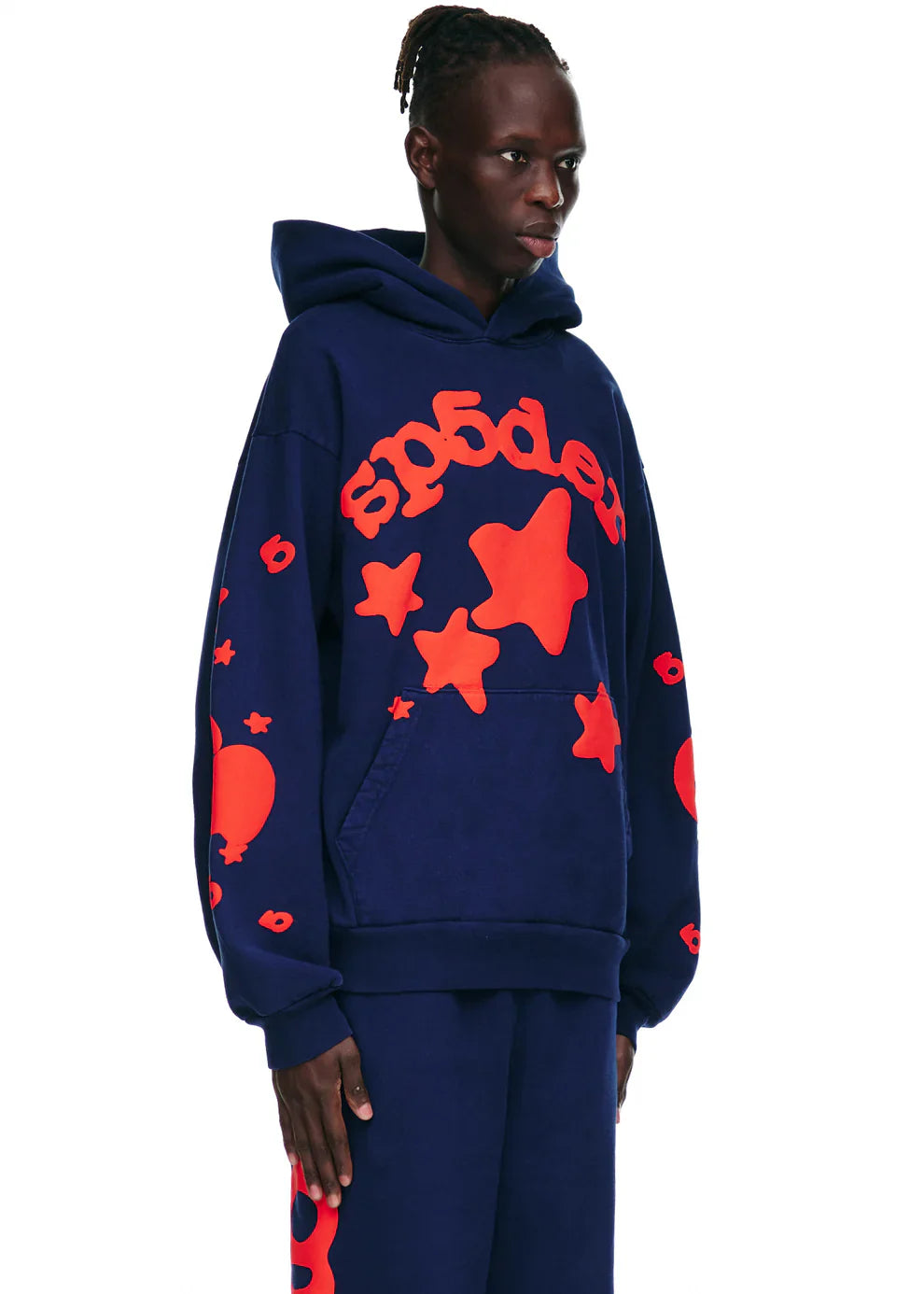 A person stands against a plain white background wearing the Sp5der 440GSM Heavyweight Hoodie in navy blue, featuring red star puff print streetwear style and bold "sp5der" lettering on the front.