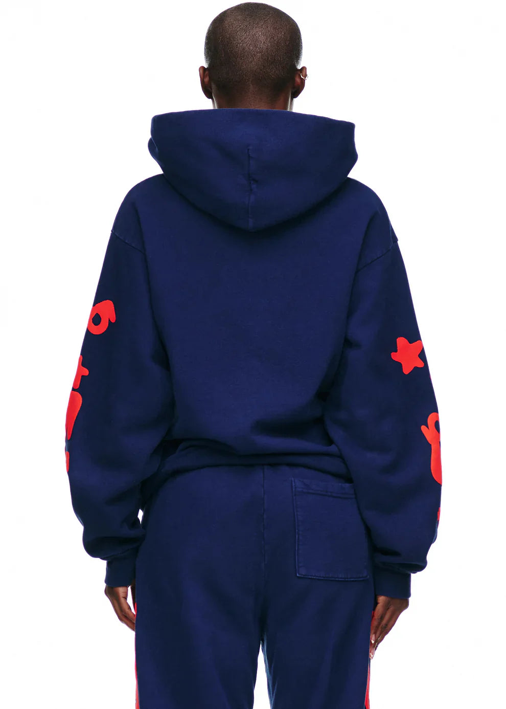 A person is seen from behind wearing the Sp5der 440GSM Heavyweight Hoodie in navy blue with red star puff print, paired with matching pants, standing against a white background.