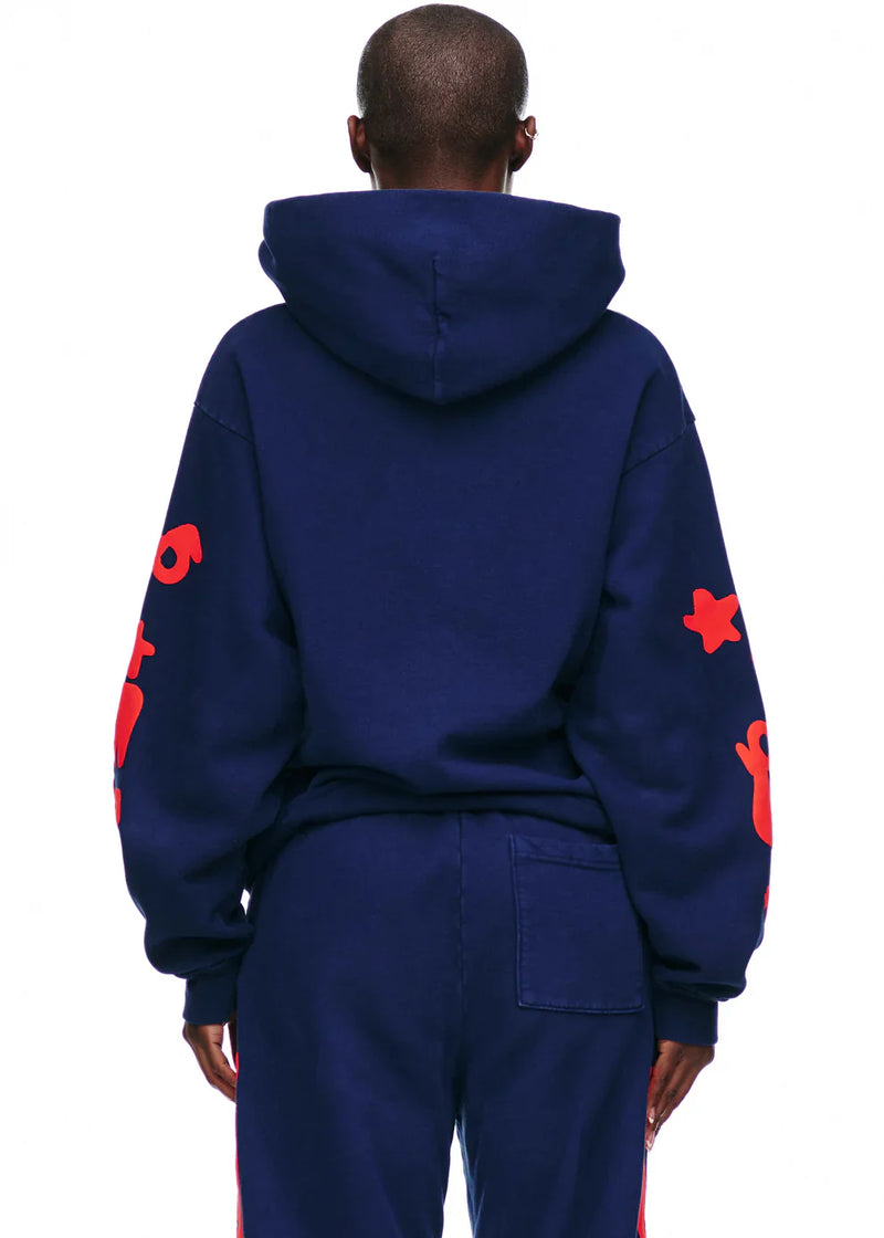 A person is seen from behind wearing the Sp5der 440GSM Heavyweight Hoodie in navy blue with red star puff print, paired with matching pants, standing against a white background.
