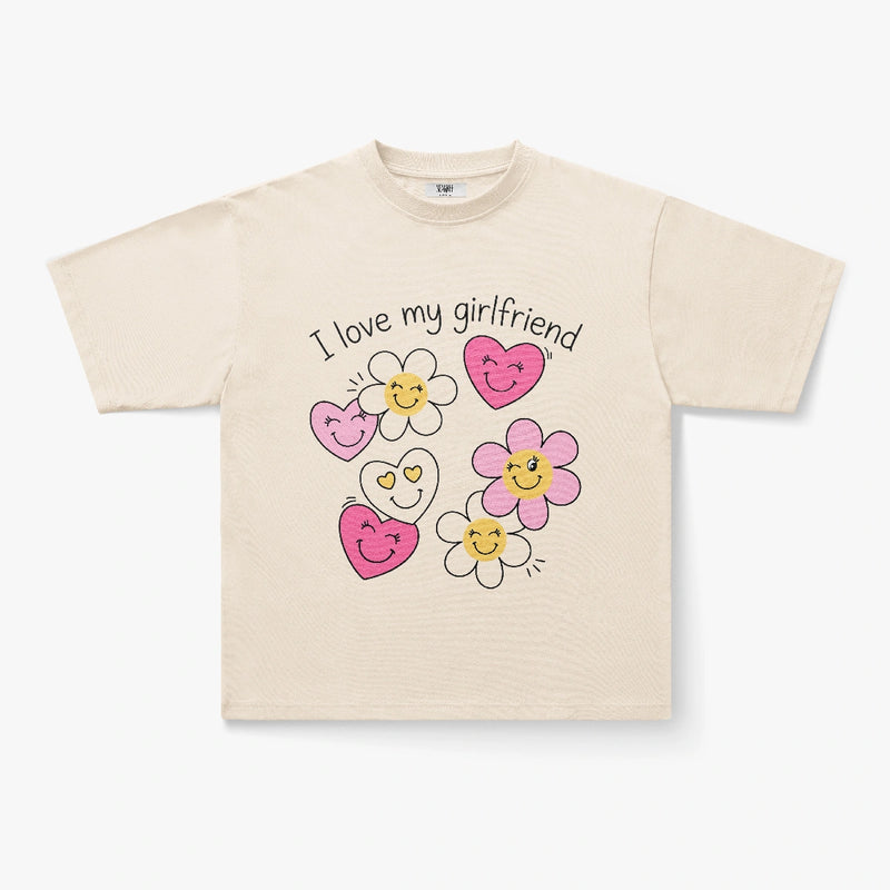 The I Love My Girlfriend Smiley Heart Daisy Graphic Print T-Shirt is a beige oversized tee with "I Love My Girlfriend" and cartoon pink and yellow flowers and hearts on the front, offering a playful Y2K vibe.
